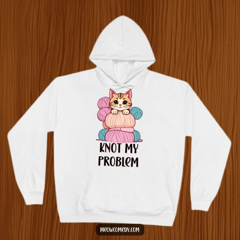 Funny cat hoodie showing a cute, mischievous cat peeking over a tall stack of colorful yarn balls with playful intent.